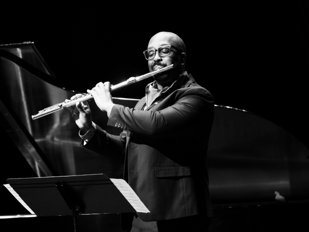 man playing flute on stage in black and white